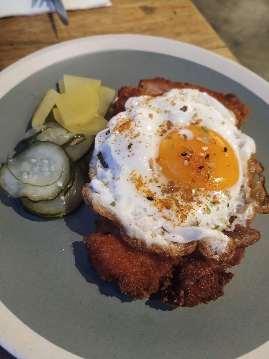 Fried cutlet topped with a fried egg, with pickled cucumber and radish