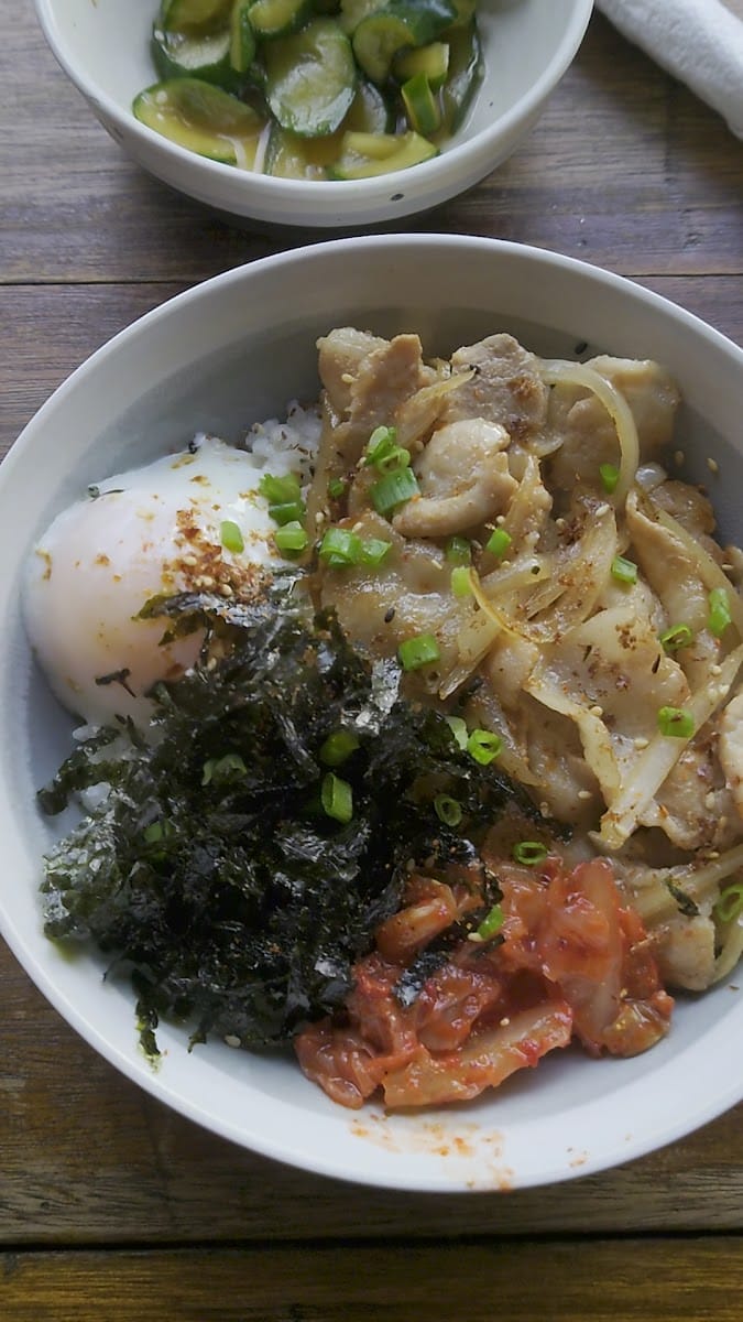 Pork donburi with a soft egg, seaweed and kimchi, and a small bowl of pickled cucumber