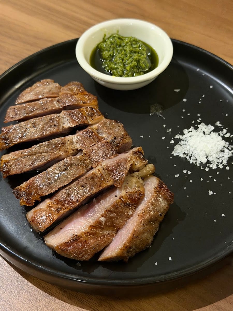Sliced grilled pork on a black plate with green sauce and sea salt